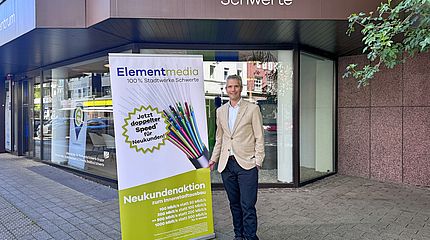Ein Mitarbeitet der Elementmedia steht vor dem Kundenzentrum der Stadtwerke Schwerte und bewirbt eine Neukundenaktion für den verkaufsoffenen Sonntag in Schwerte