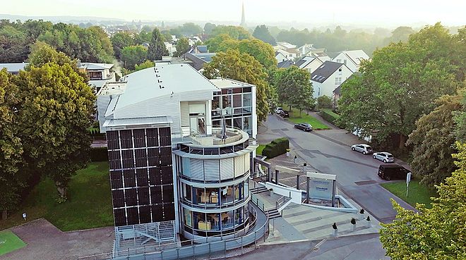 Hauptgebäude der Stadtwerke Schwerte: Verwaltungsgebäude mit Glassfassade umgeben von Bäumen, davor Parkplätze mit Elektroladesäulen