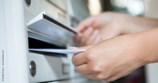 Eine Hand steckt einen Brief in einen privaten Briefkasten mit mehreren Fächern