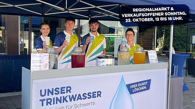 Drei Personen in weißen Poloshirts mit grünen und gelben Streifen stehen hinter einem Stand mit Wasserspendern und Getränkekrügen, beworben wird Trinkwasser für Schwerte mit Hinweis auf Regionalmarkt am 22. Oktober