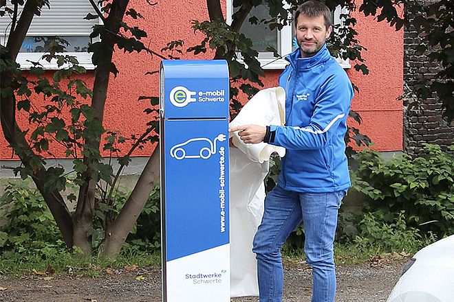 Ein Mitarbeiter der Stadtwerke Schwerte in blauer Arbeitskleidung vor einer e-Ladesäule der Stadtwerke