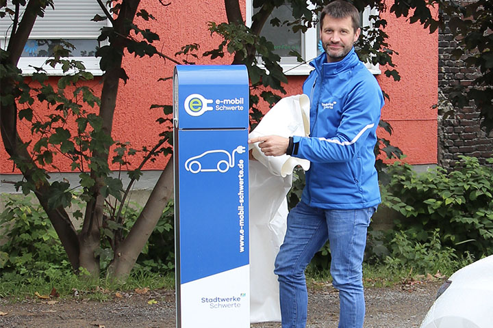 Ein Mitarbeiter der Stadtwerke Schwerte in blauer Arbeitskleidung vor einer e-Ladesäule der Stadtwerke