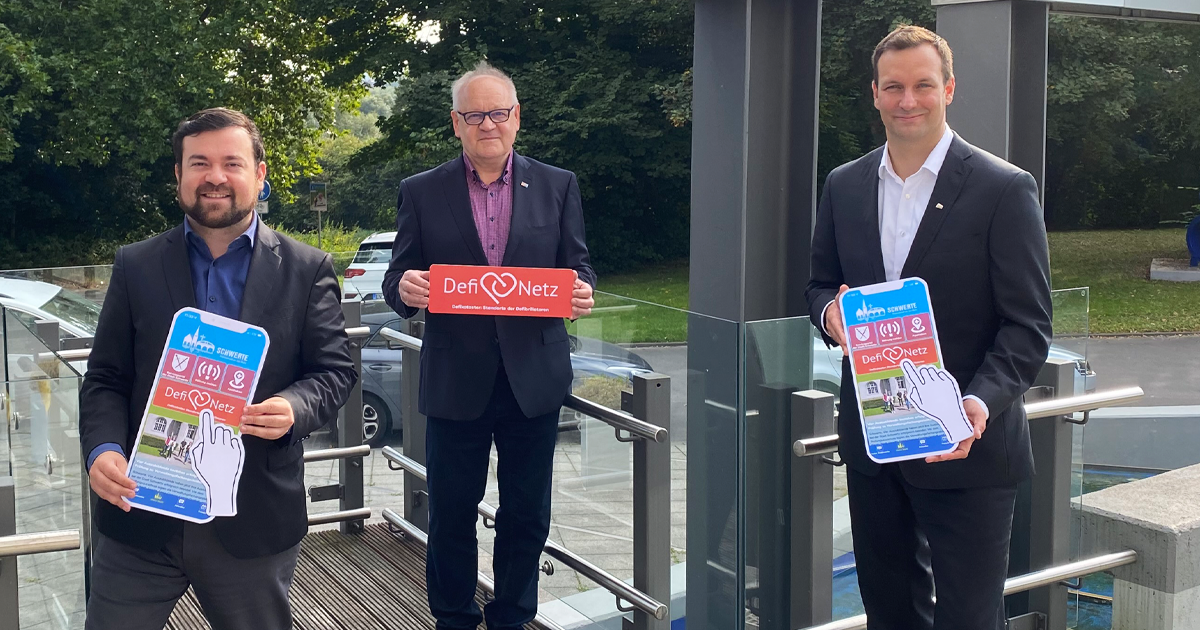 Bild von Bürgermeister Dimitrios Axourgos, ehemaliger 1. stellvertretender Bürgermeister Jürgen Paul und Geschäftsführer der Stadtwerke Schwerte GmbH Sebastian Kirchmann, die Papphandys symbolisch für die Schwerte App in die Kamera halten