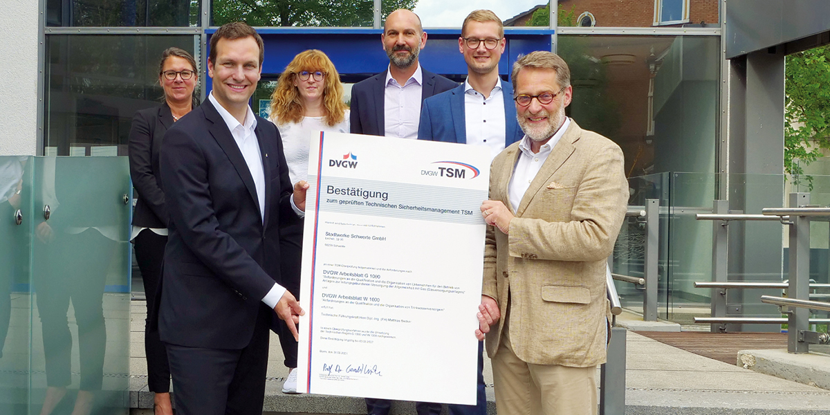 Sebastian Kirchmann, Geschäftsführer der Stadtwerke Schwerte, und Dr. Bernhard Klocke vom DVGW halten gemeinsam das Zertifikat "Bestätigung zum geprüften Technischen Sicherheitsmanagement TSM" hoch, im Hintergrund vier weitere Mitarbeiter der Stadtwerke Schwerte