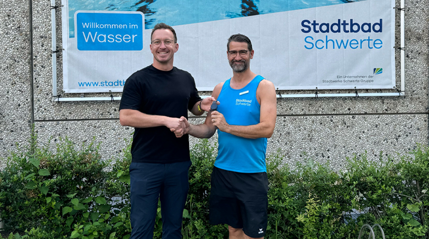 Zwei Personen vor dem Stadtbad Schwerte. Sie geben sich die Hände und Florian Grojer übergibt eine KI-Uhr Anden ehemaligen Schwimmbadleiter Thomas Jeserig.