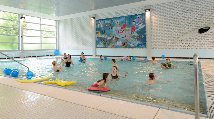 Innenansicht des Stadtbad Schwerte. Zu sehen ist das Kinderbecken mit mehreren Kindern und Spielgeräten im Wasser.