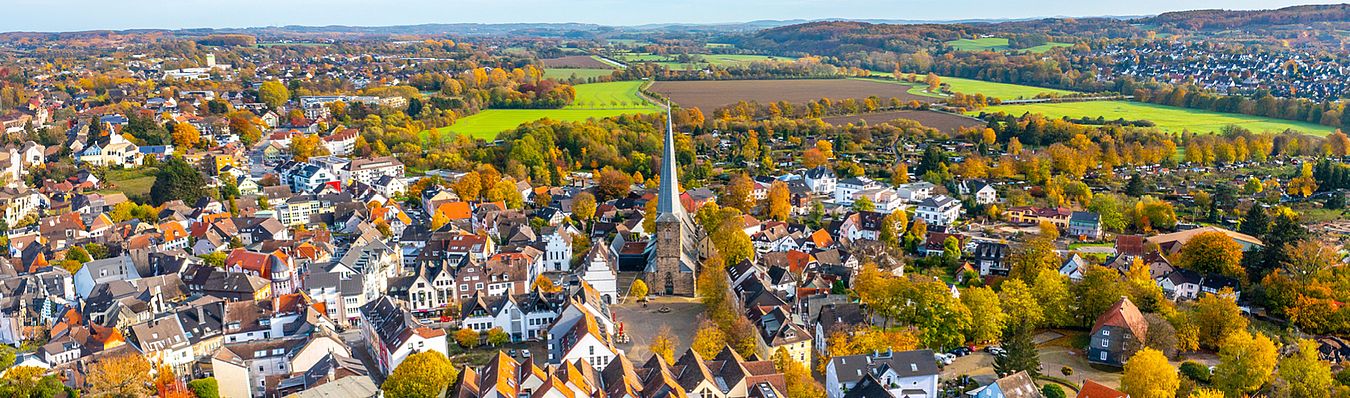 Luftaufnahme der Stadt Schwerte mit der Ev. Kirche St. Viktor sowie dem Marktplatz im Mittelpunkt, umgeben von zahlreichen Häusern sowie grünen Feldern im Hintergrund.