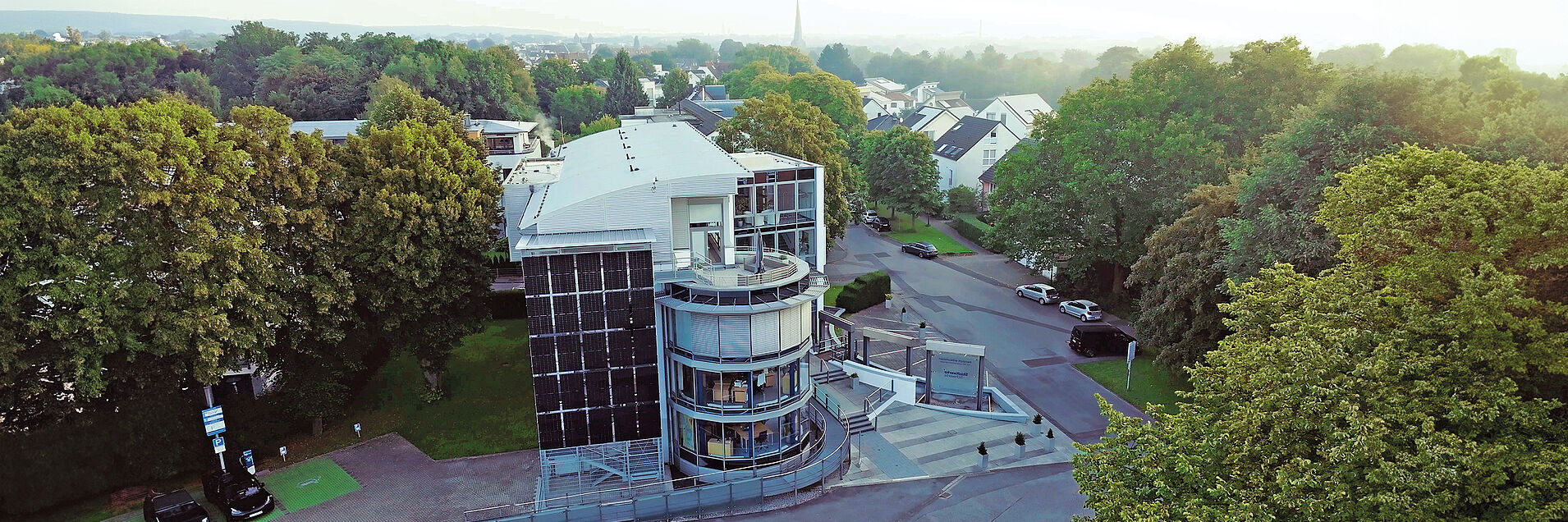Hauptgebäude der Stadtwerke Schwerte: Verwaltungsgebäude mit Glassfassade umgeben von Bäumen, davor Parkplätze mit Elektroladesäulen